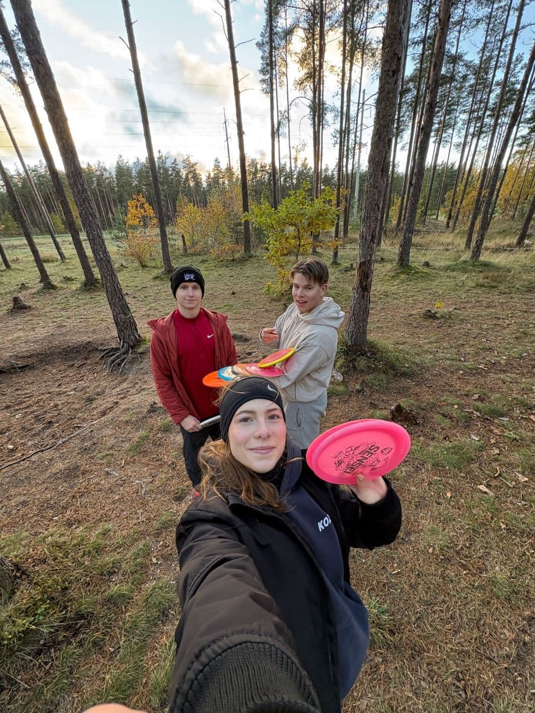Kolm sõpra discgolfi mängimas männimetsas